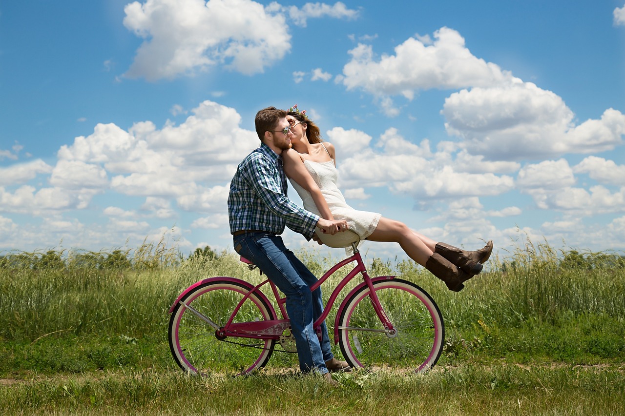 Descubre la alegría de una pareja en bicicleta en un día soleado, rodeados de naturaleza y nubes dispersas en el campo